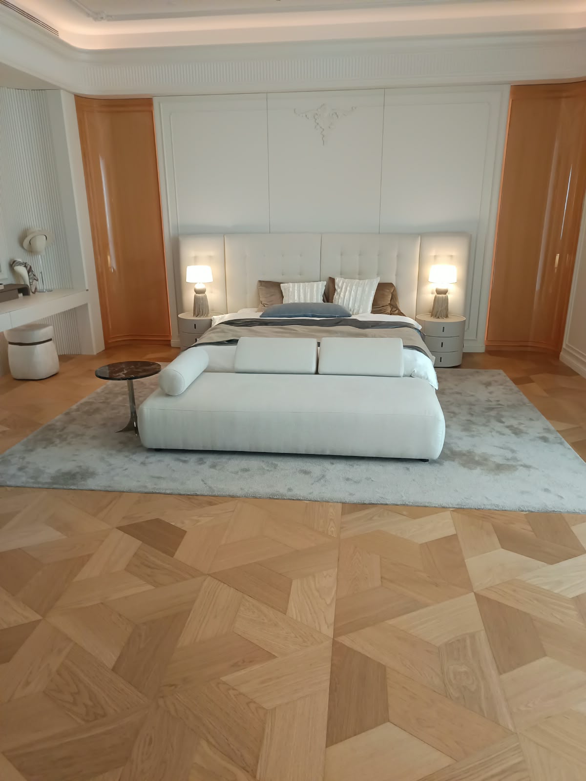 Luksuzna hotelska spalnica s širokim oblazinjenim vzglavjem, klopjo in geometrijskim parketom
